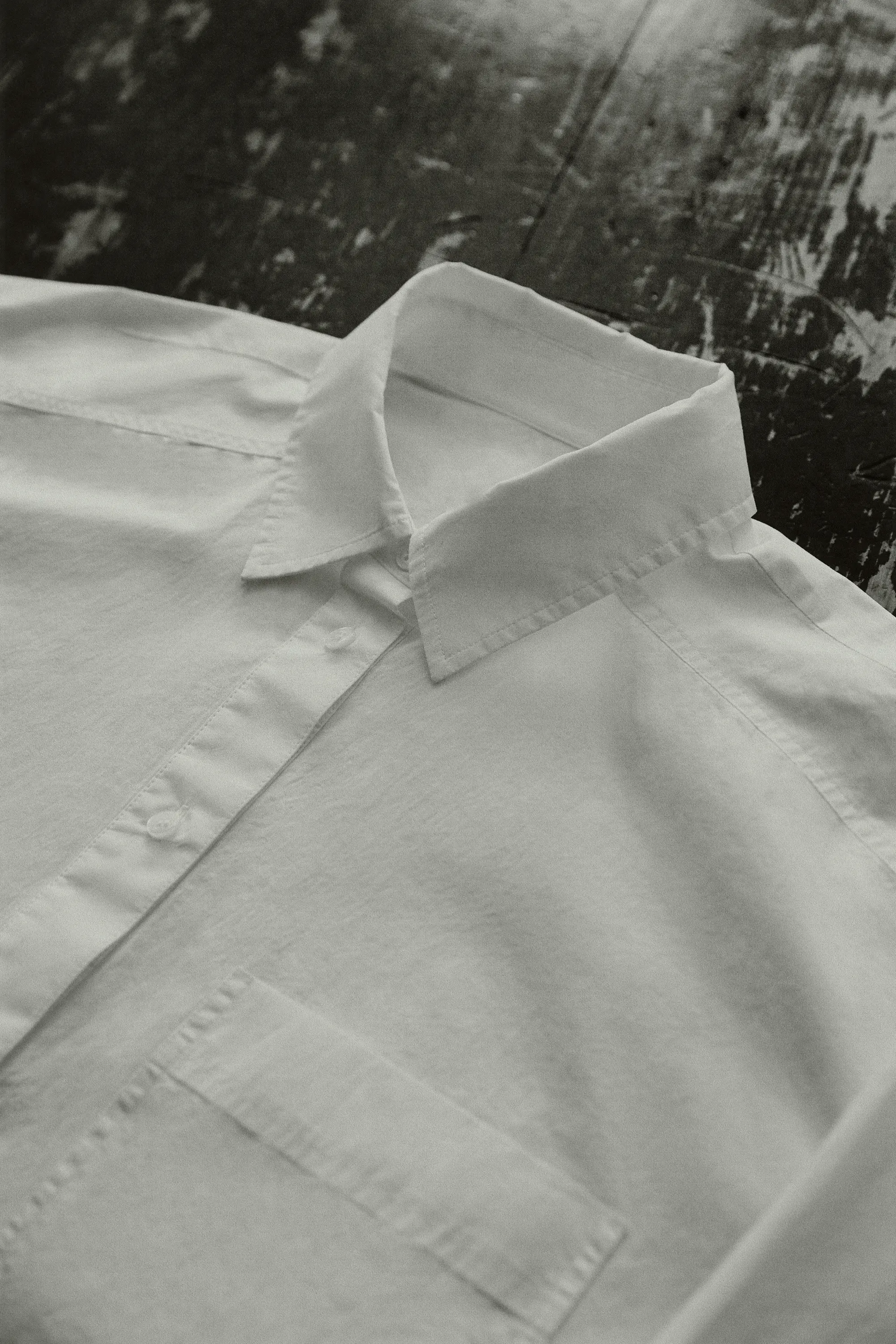 Studio product shot of a white collared dress shirt with buttons and chest pocket, photographed on a dark scratched wood surface.