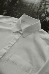 Close-up of a white collared button-down shirt resting on a dark distressed wooden surface.