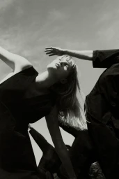 Monochrome low-angle fashion shot of a blond woman in a black garment posing dramatically against a clear sky