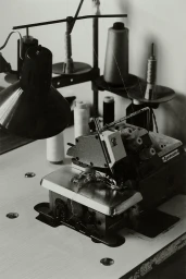 Close-up of a vintage industrial sewing machine on a light workbench with spools of thread and an adjustable lamp in the background.