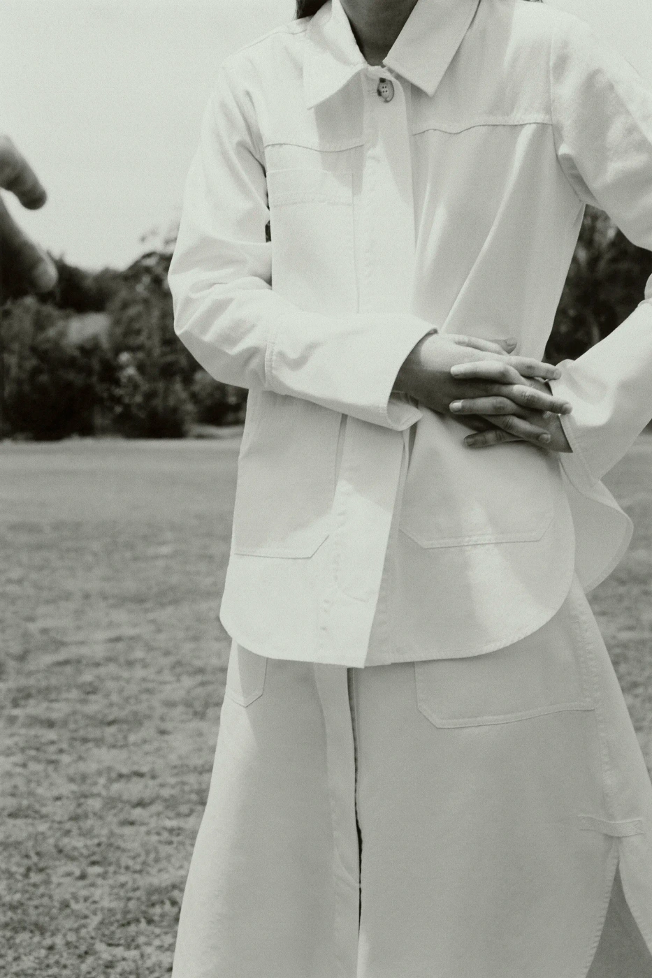 Model wearing a white shirt and skirt standing outdoors on grass
