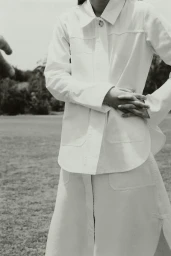Model wearing a white shirt and skirt standing outdoors on grass