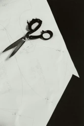 Black tailoring scissors resting on a white paper sewing pattern featuring handwritten annotations.