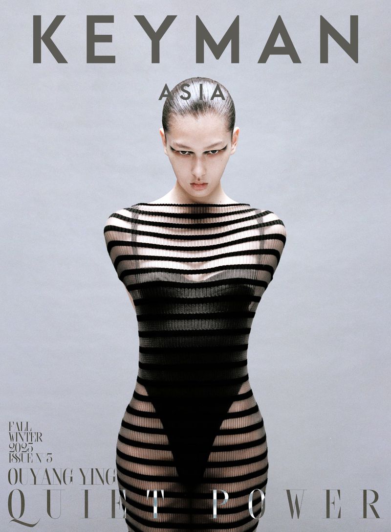 Magazine cover featuring a slender adult female fashion model in a horizontally striped black sheer dress against a gradient grey background.
