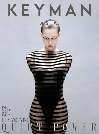 Magazine cover featuring a slender adult female fashion model in a horizontally striped black sheer dress against a gradient grey background.