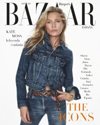 Kate Moss posing in a double denim trucker jacket and jeans with a brown leather belt on a plain white studio background.