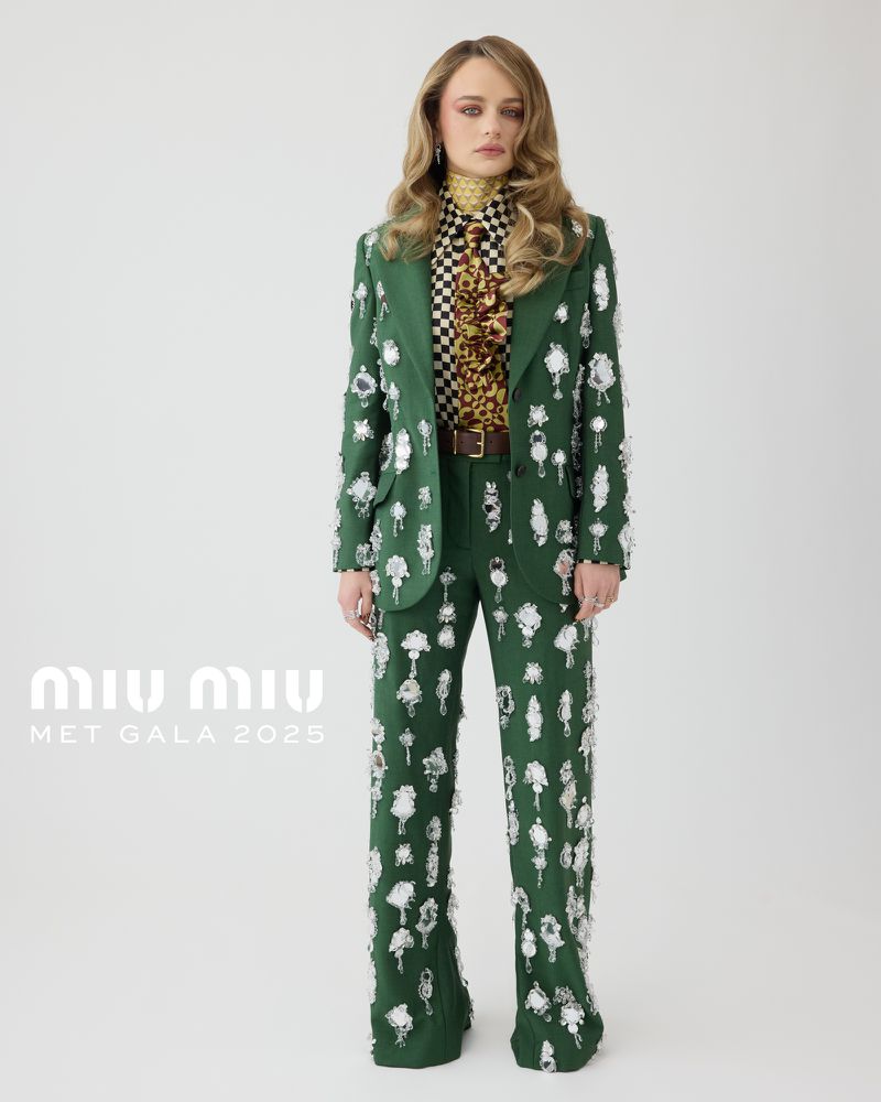 Model posing in green Miu Miu pantsuit with embellishments, paired with patterned top, in a fashion forward full-length studio shot.