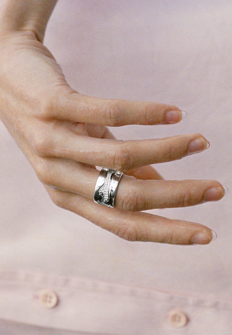 Close-up of a hand wearing a wide sculptural silver band with pave stones resting over a light pink button-down shirt.