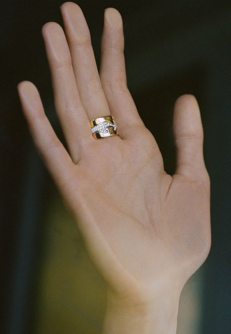 Hand wearing a gold ring with diamonds, studio lighting, neutral background, jewelry advertisement, close-up shot, luxury style.