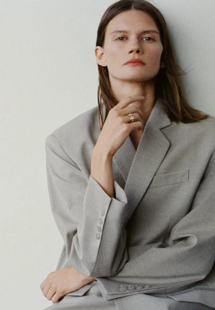 Daniela Kocianova wearing an oversized light grey tailored blazer and a gold ring against a neutral background.