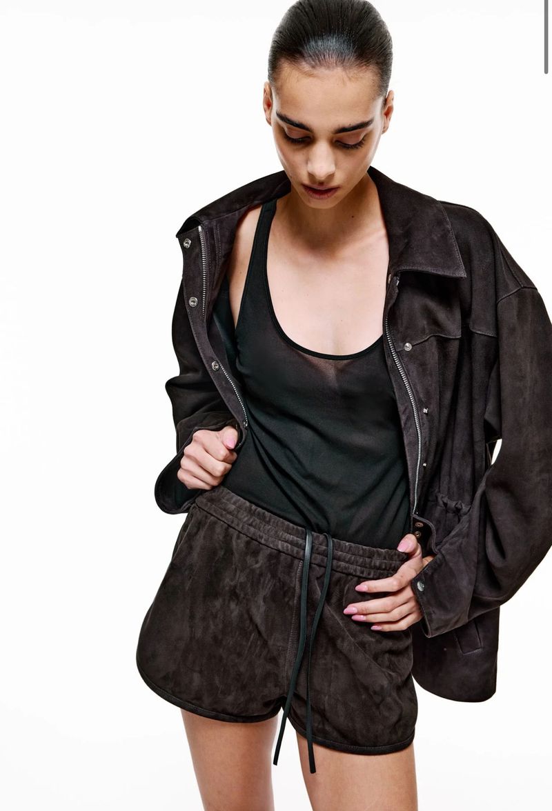 Model wearing a dark brown suede jacket, matching shorts, and a black tank top against a white studio background.