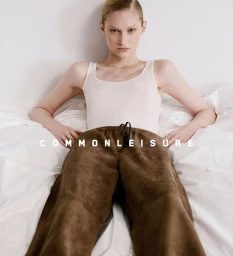 Model wearing a white tank top and brown trousers posing on white bedding for Common Leisure SS25