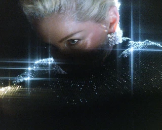 Close-up of a blonde woman wearing a dark sparkling top and crystal earrings with starburst light streaks.