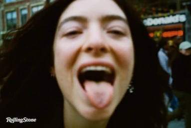 Close-up portrait of singer Lorde sticking her tongue out with dark wavy hair on a city street for Rolling Stone.