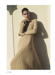 Model Anthi Fakidari wearing a long-sleeve beige ribbed knit maxi dress against a sunlit wall for Elle Germany.