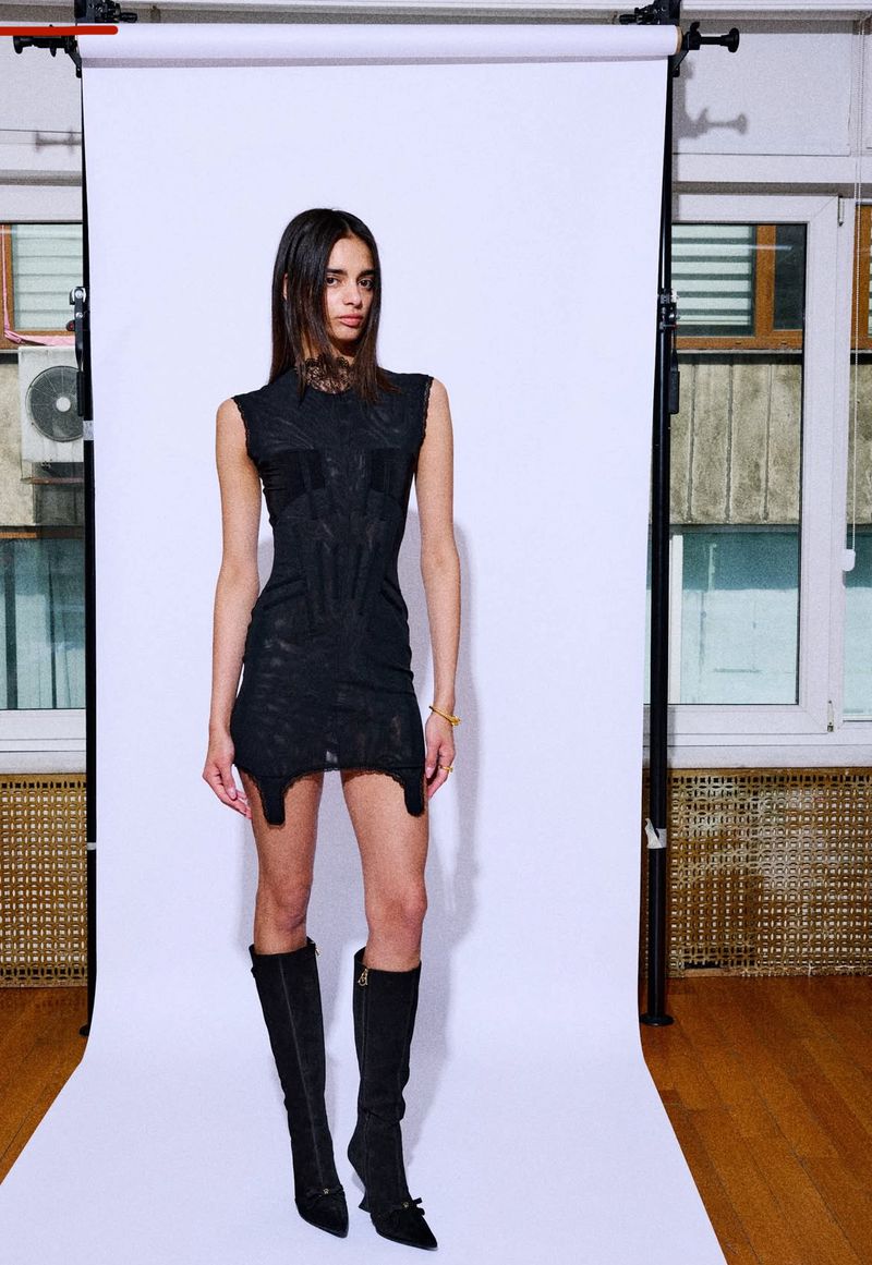 Full-length portrait of a young woman in black mini dress and knee-high boots against a white backdrop in a well-lit photo studio.