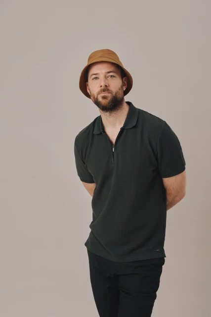 A man in a bucket hat and polo shirt poses against a neutral background, looking directly at the camera in a portrait-style photograph.