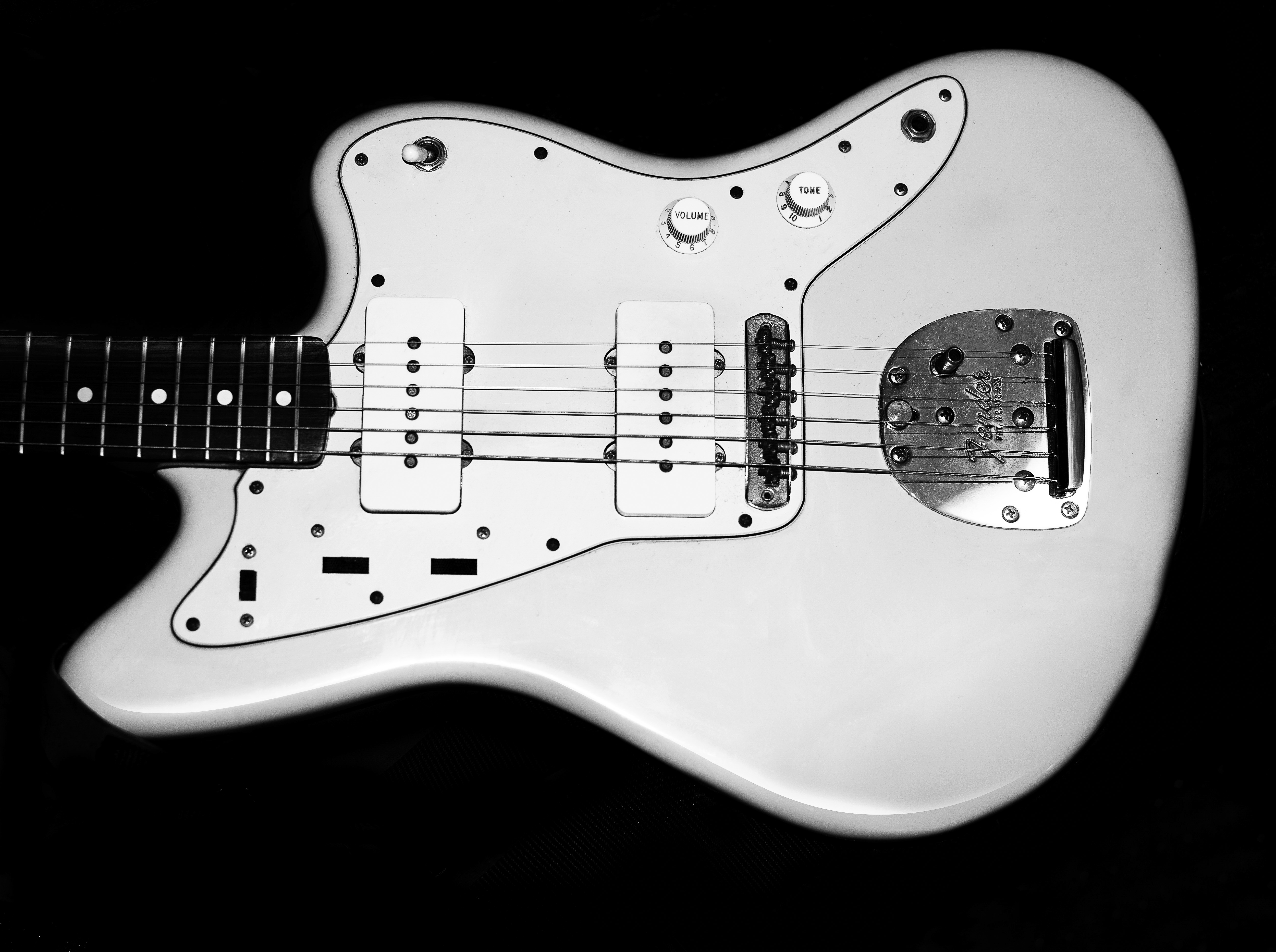 Electric guitar with a white body and black fretboard shown in a studio shot against a black background with clear volume and tone knobs.