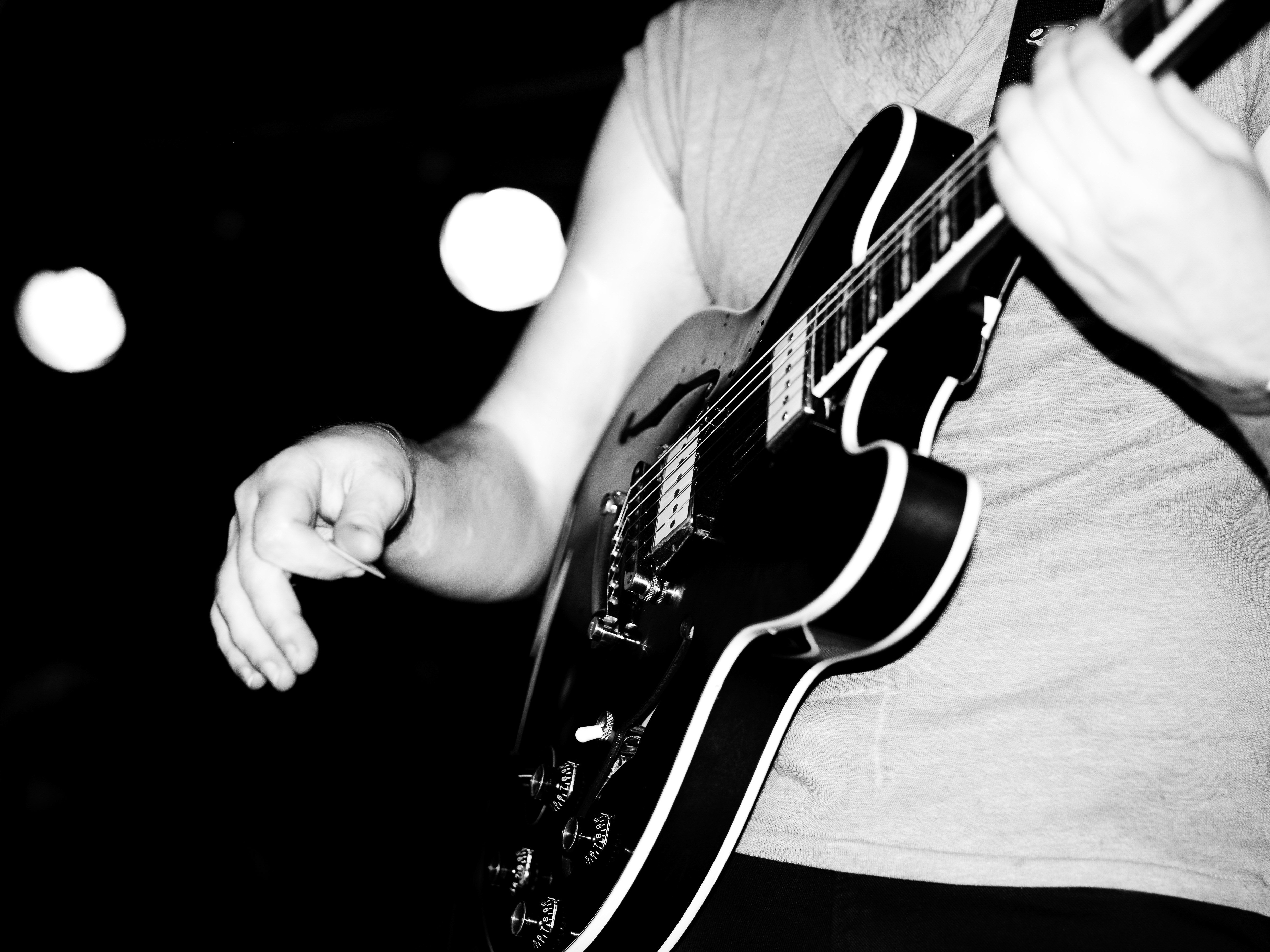 A musician plays an electric guitar in a monochrome image, showing the guitar's body, neck, and strings, along with the performer's hand.