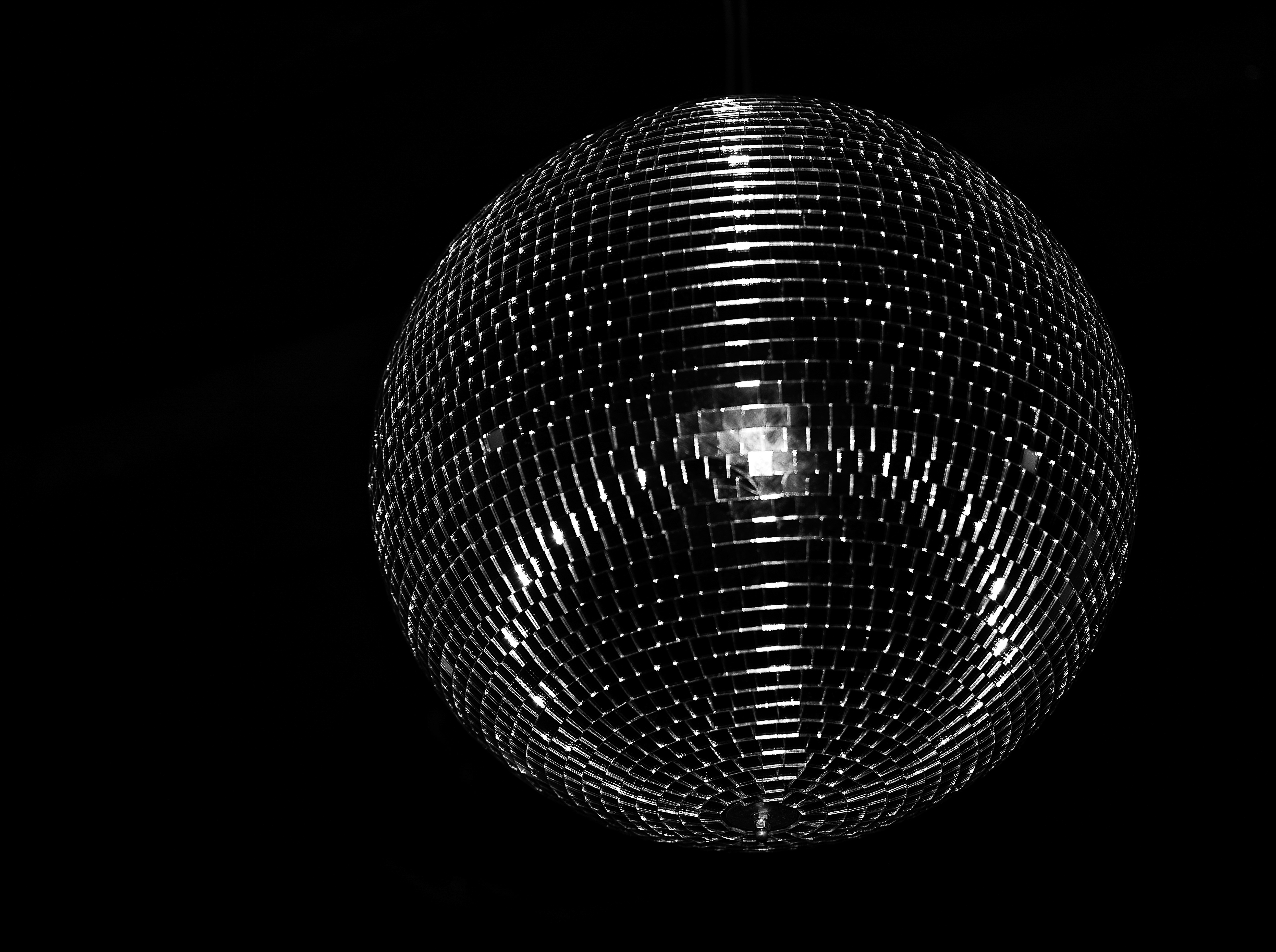 Shiny disco ball hanging in a dark space, reflecting light from its mirrored tiles in a monochrome, black-and-white scene.