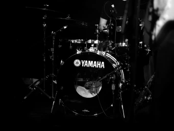 Monochrome close-up of a Yamaha bass drum kit and cymbals with studio microphones in dramatic low-key lighting.