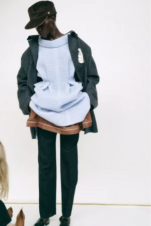Model wearing a structured dark coat, light blue sweater, and brown cap against a white background for WSJ.