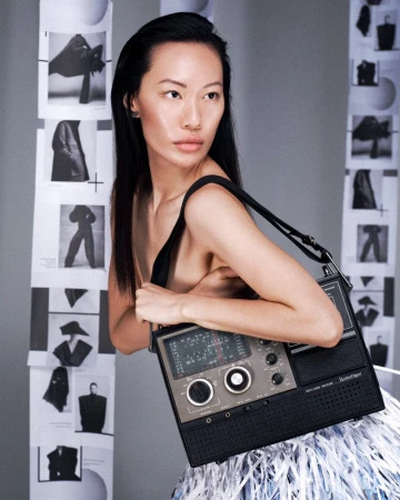 Asian woman in a fashion portrait holding a vintage radio-style handbag, posing against a backdrop of black and white fashion photos.