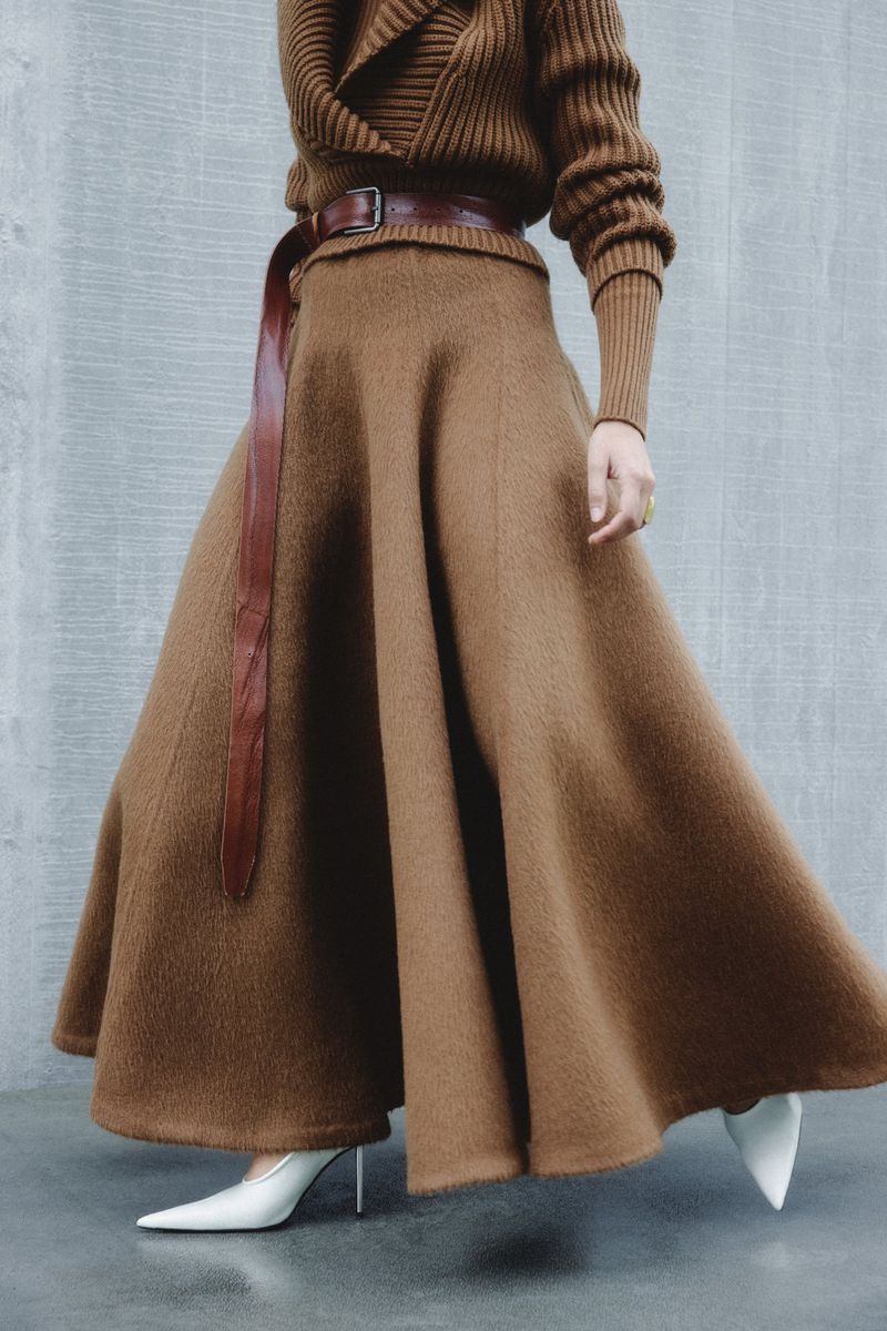 Fashionable adult female showcasing a brown sweater and matching wool skirt with a brown belt, paired with white high heels.