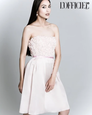 Elegant woman in a light pink strapless dress posing in a studio, long dark hair, minimalist earrings, light grey background.