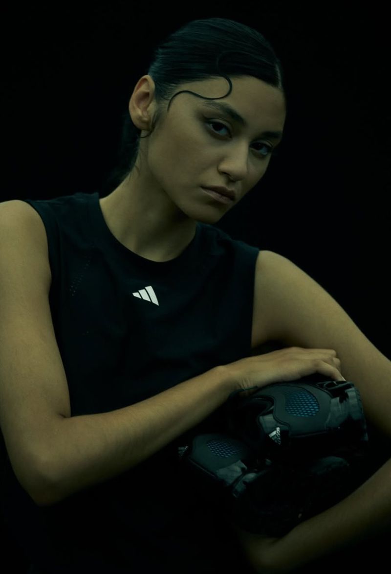 A woman in athletic wear holds a football in a dark studio setting, showcasing a sporty and modern aesthetic with focus on the subject.