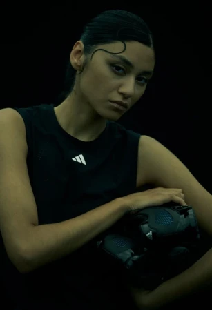 A woman in athletic wear holds a football in a dark studio setting, showcasing a sporty and modern aesthetic with focus on the subject.