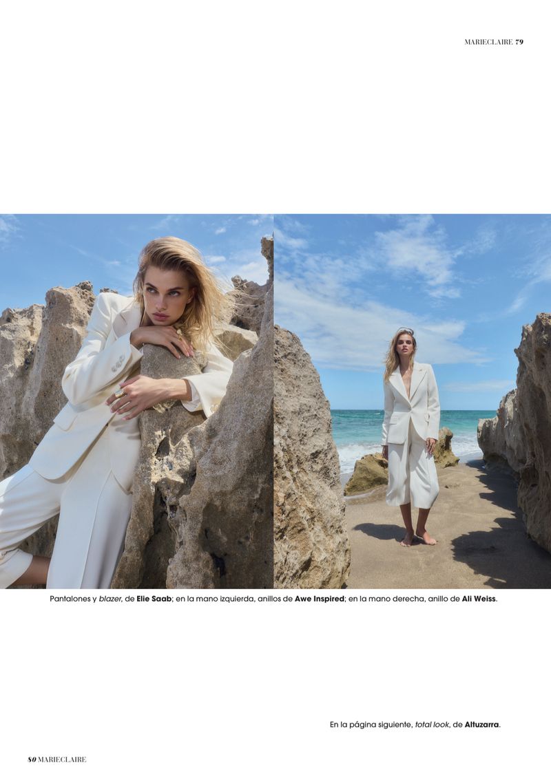 A woman in a white suit poses by rock formations near the ocean on a sunny day in a fashion editorial shot for Marie Claire.