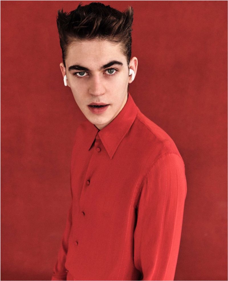 Studio portrait of a young adult male in a red shirt with light skin, dark hair, and earbuds, set against a red backdrop.