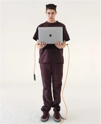Hero Fiennes Tiffin holding a laptop with orange cords attached against a plain white background for GQ Australia