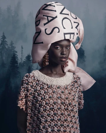 Portrait of a dark-skinned woman wearing a beaded top and a large hat with text, set against a misty forest backdrop.