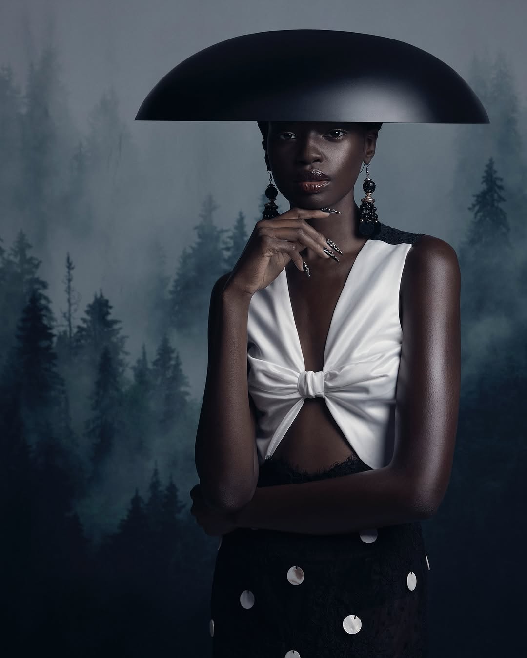 Striking portrait of an African American woman wearing formal attire and statement earrings against a moody forest backdrop.