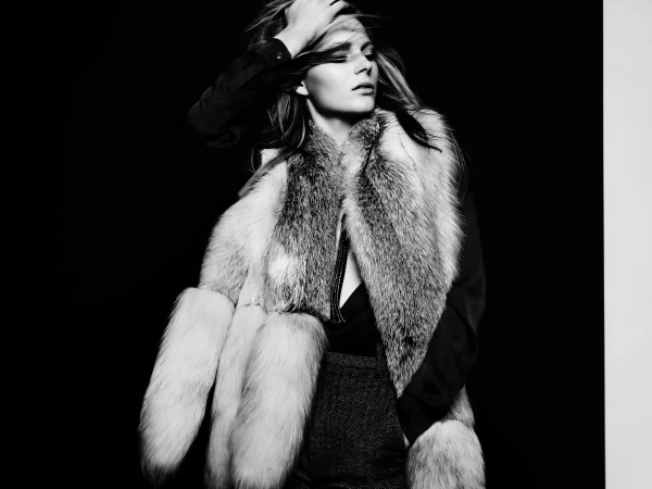 Black and white portrait of a blonde woman in a fur vest, captured in a studio setting with a dark backdrop, fashion, and luxury appeal.