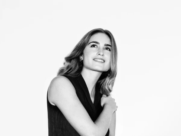 Black and white portrait of a smiling woman with long brown hair wearing a sleeveless black top, looking up and to the left.
