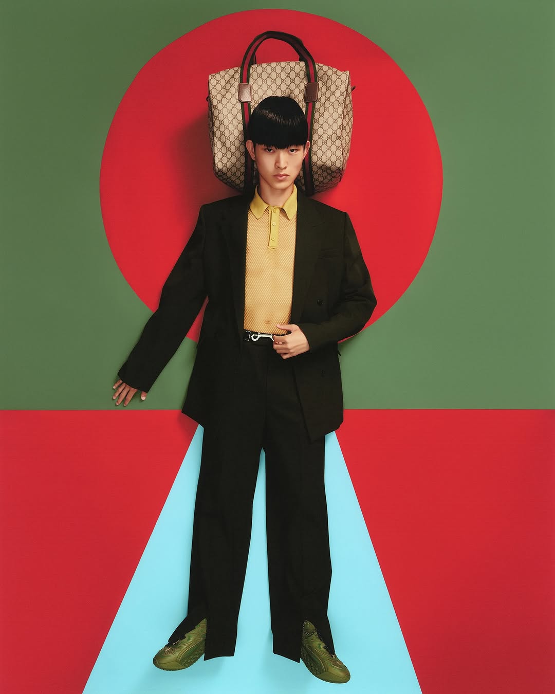 Person in black suit with a Gucci bag posing in front of red, green, and blue geometric background. Fashion editorial photography.