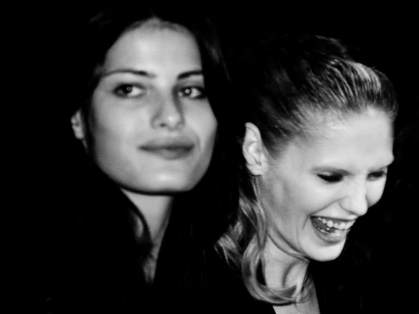 Black and white shot of two fair-skinned adult women, one with a neutral expression and the other laughing with head turned to the side.