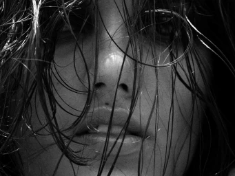 Close-up black and white portrait of a person's face obscured by wet, tangled strands of hair across the eyes and nose.