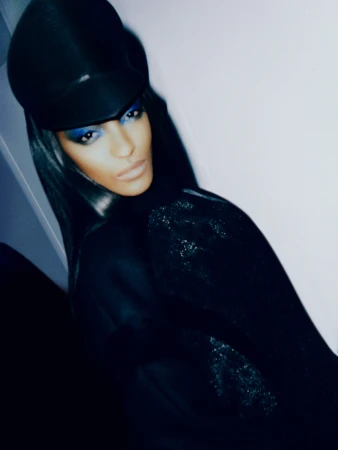 Close-up portrait of a stylish adult female with dark hair, wearing a black hat and black clothing with blue eyeshadow makeup.
