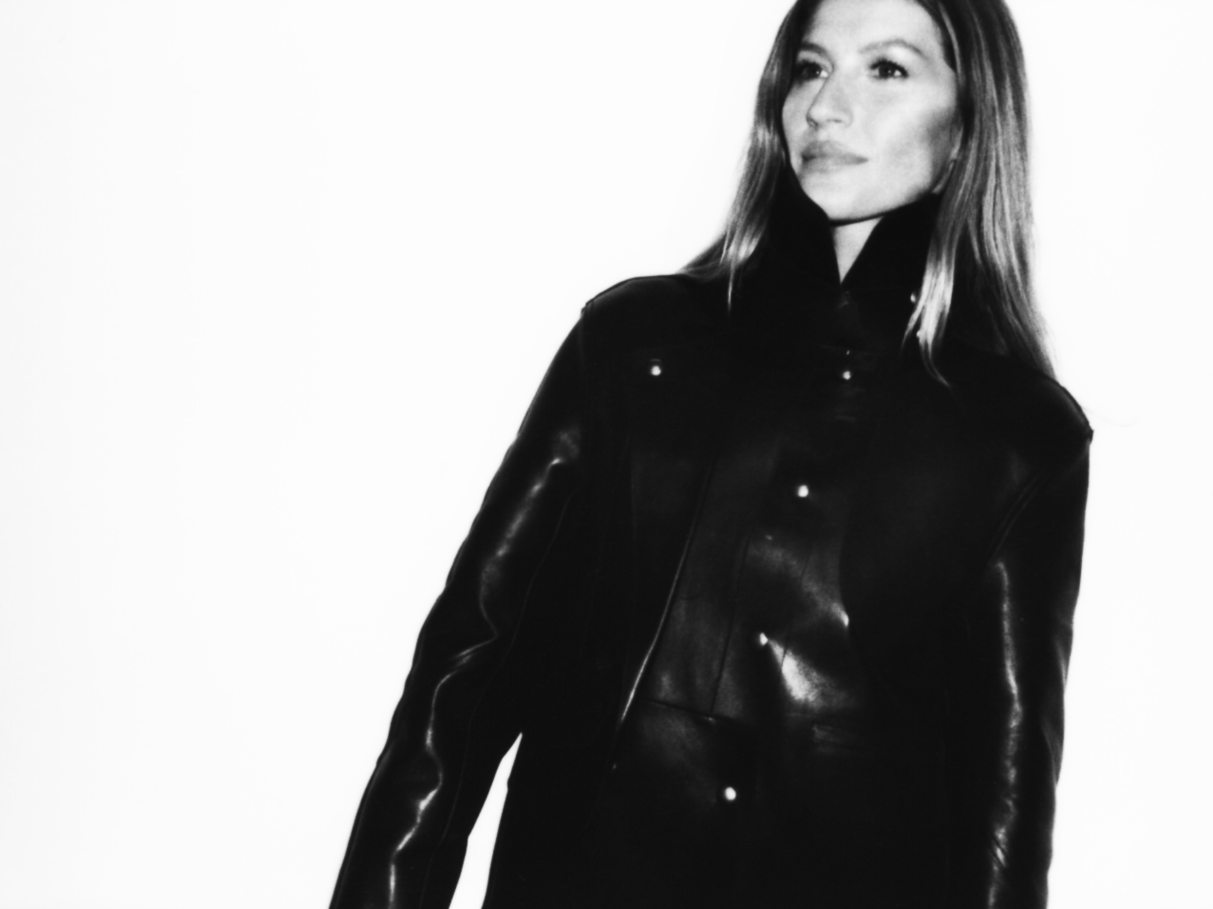 A light-skinned woman with long hair is looking off to the side while wearing a black leather jacket in a studio setting.