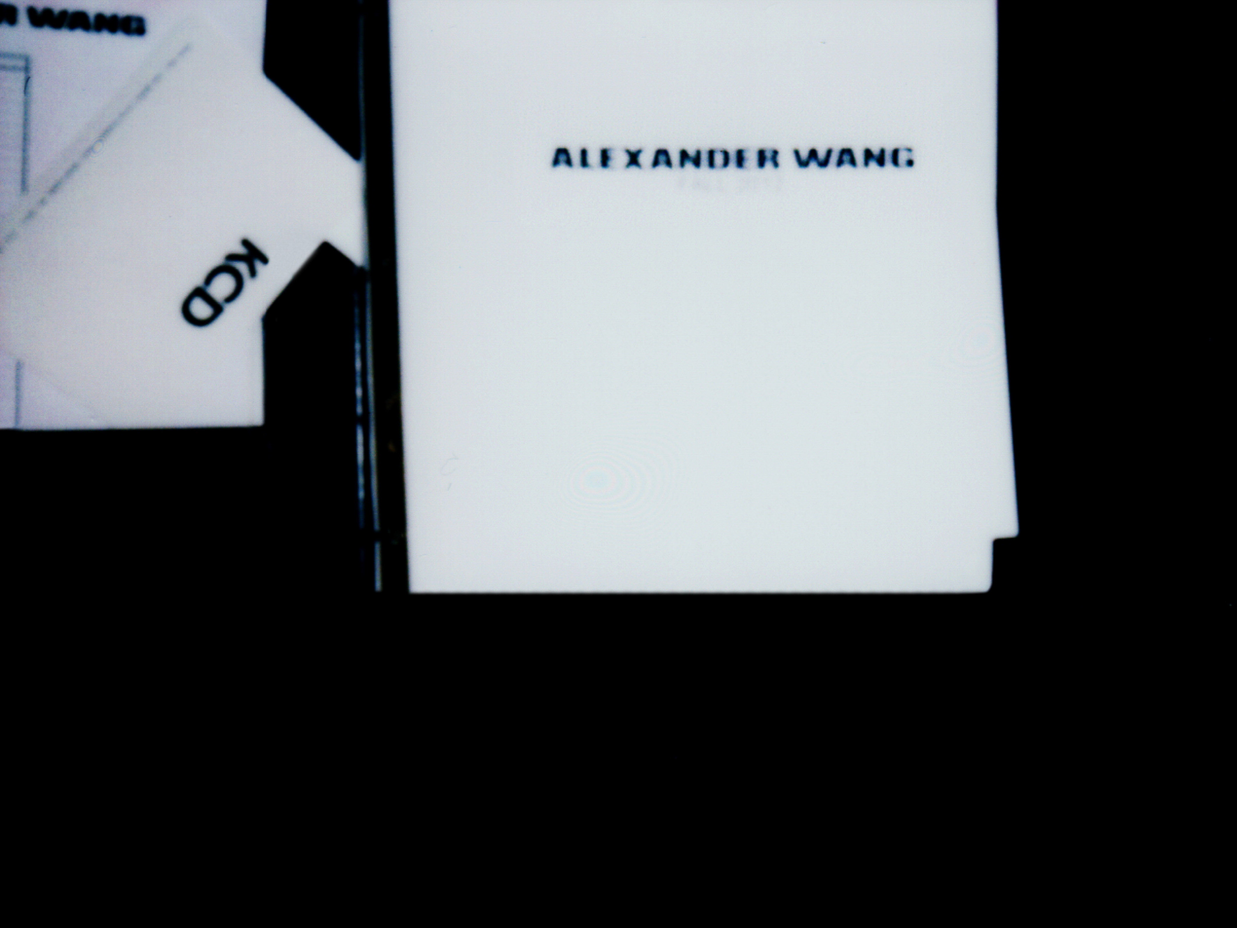 Close-up of white cards against a black background, with the text 'ALEXANDER WANG' visible on one of the cards.