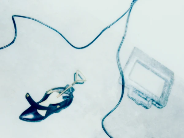 High-angle shot of a dark shoe with shoe stretcher, cord, and picture frame against a white backdrop with minimalist composition and blue tones.