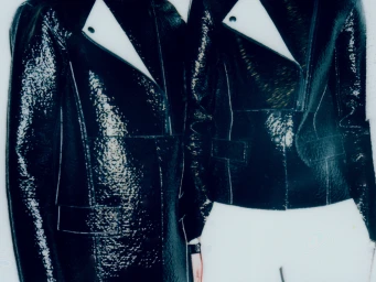 Two individuals wearing glossy black jackets with white lapel accents against a minimalist white background