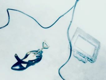 Overhead studio view of a black shoe, shoehorn, and cords on a pale floor