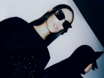 Model wearing dark sunglasses and black clothing against a white background by Cameron Krone for New York Times Style