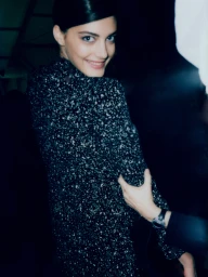 A woman wearing a dark tweed jacket smiling over her shoulder backstage for New York Times Style by Cameron Krone.