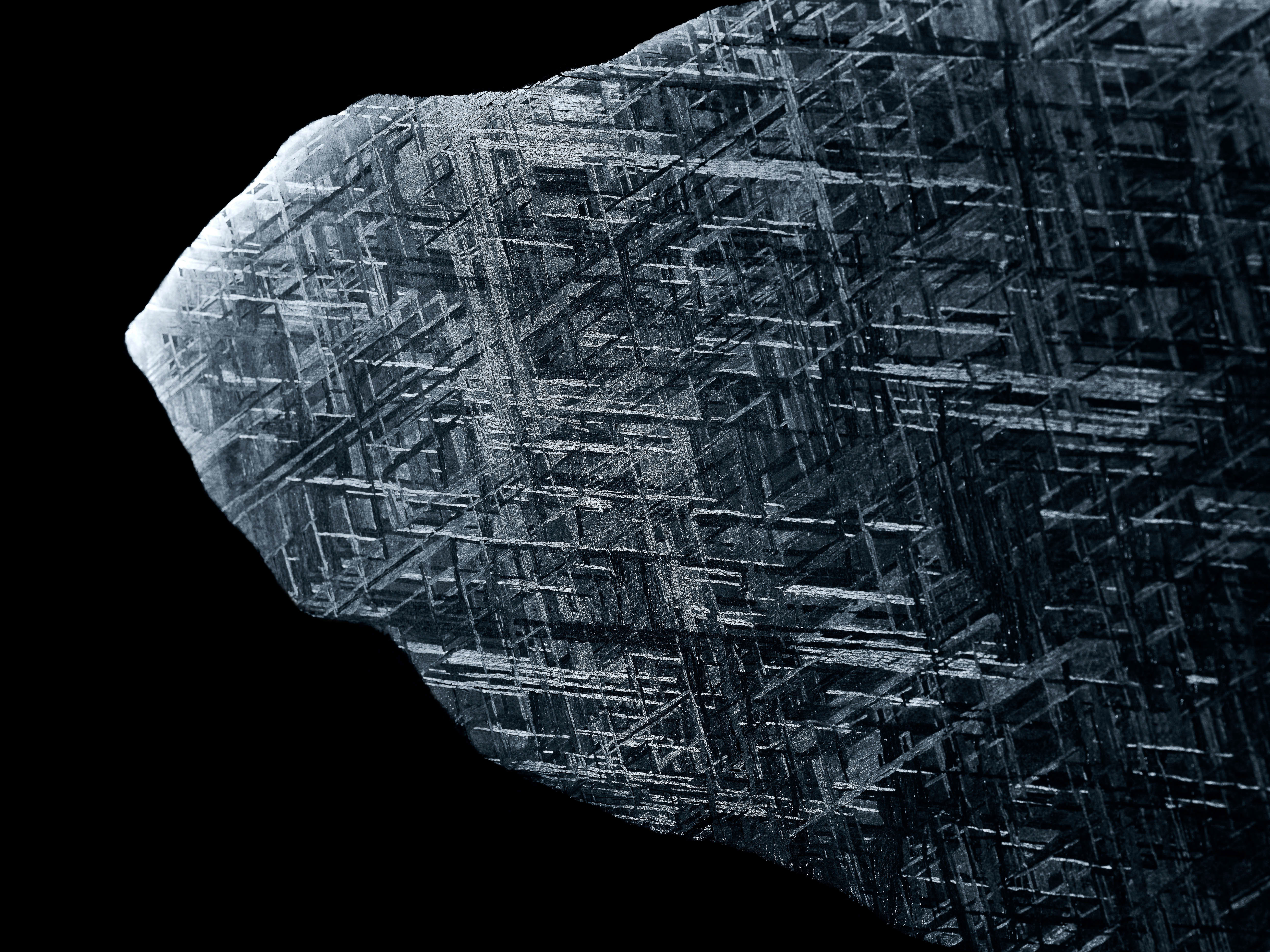 Detailed macro photograph of the Widmanstätten pattern in a meteorite fragment against a solid black backdrop, showcasing its intricate texture.